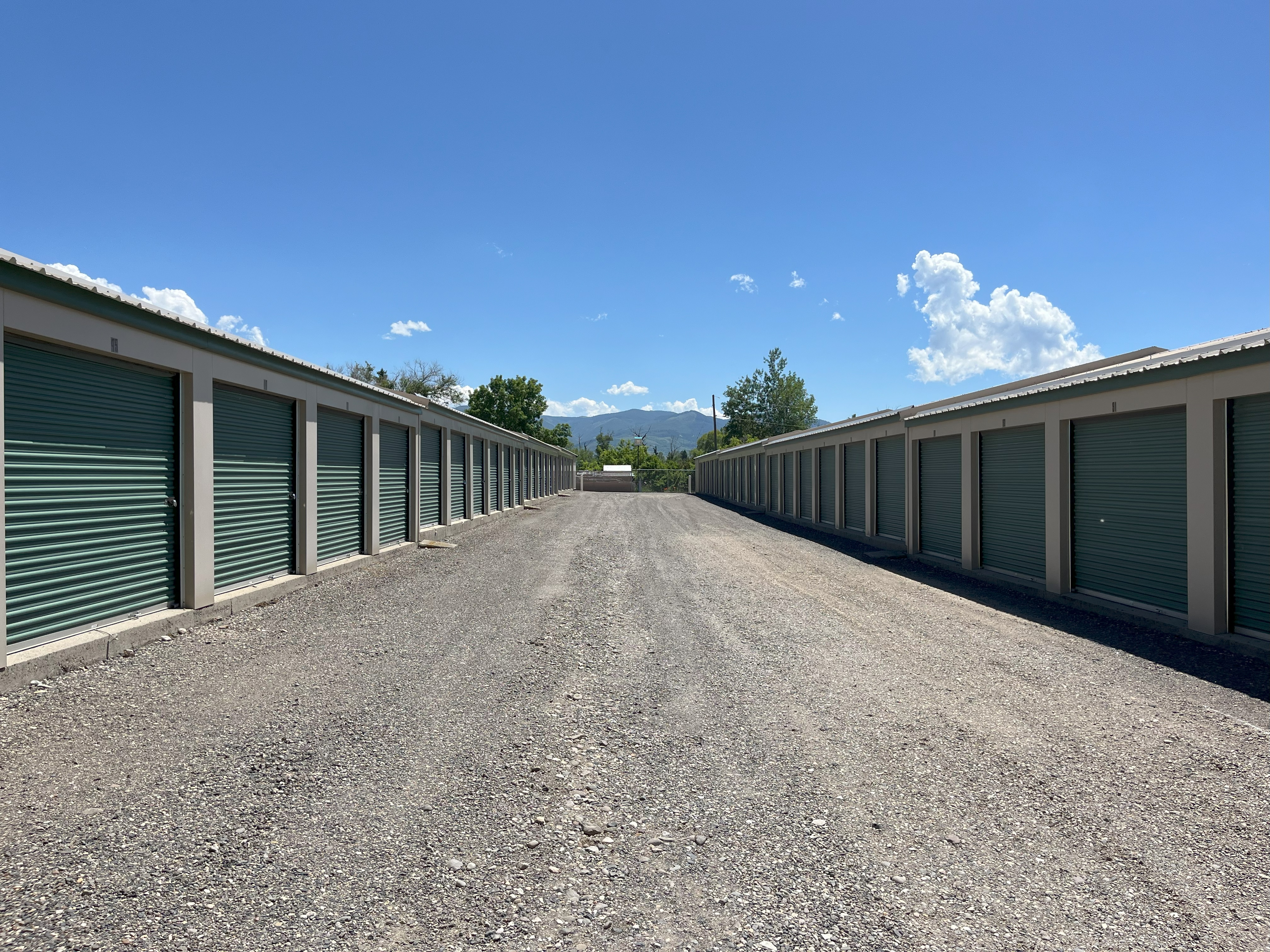 wide gravel drive at Alpine Storage MT with tan buildings and green garage doors